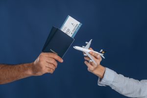 Close-up of male and female hands holding flight tickets and a toy airplane, symbolizing travel planning and upcoming vacation.