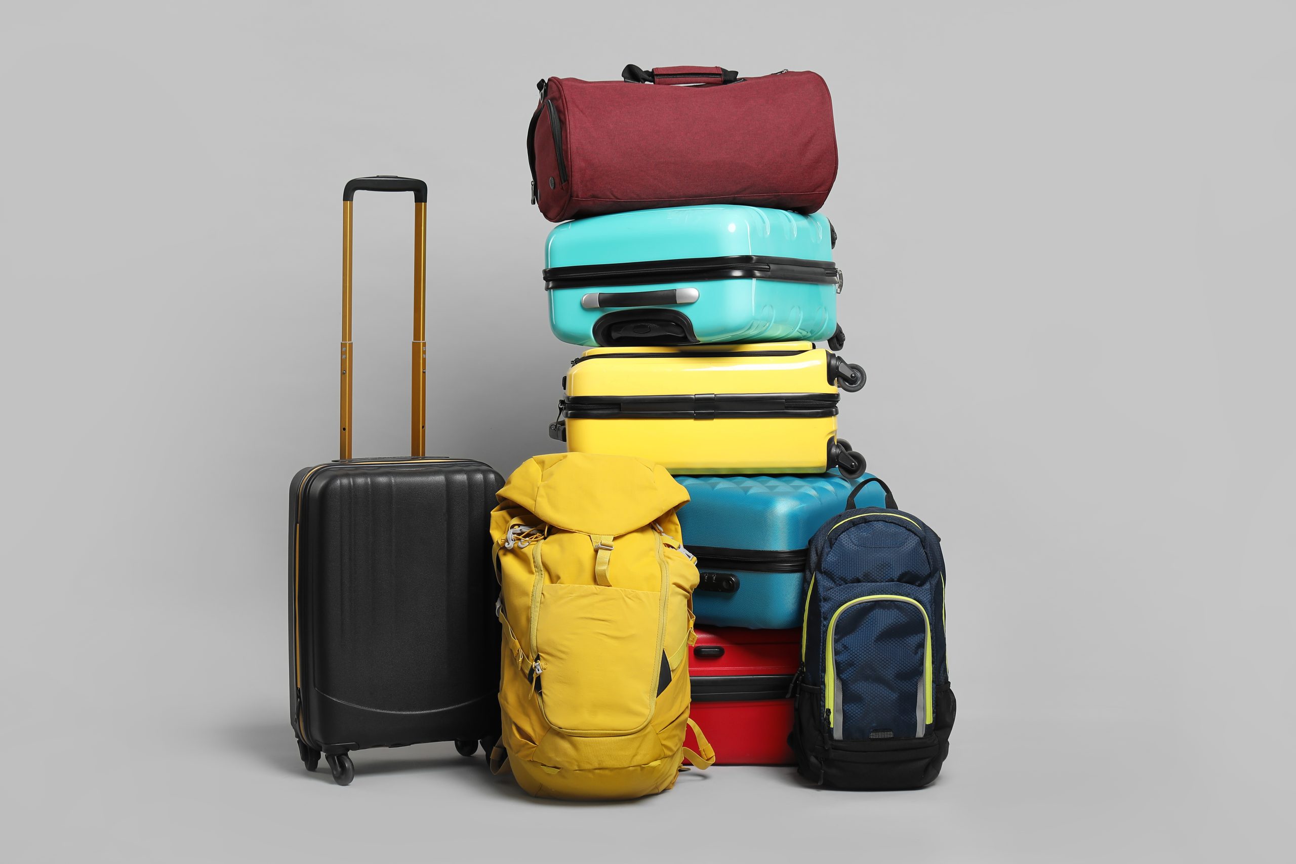 A collection of multicolored suitcases and bags arranged in a pile on a grey background
