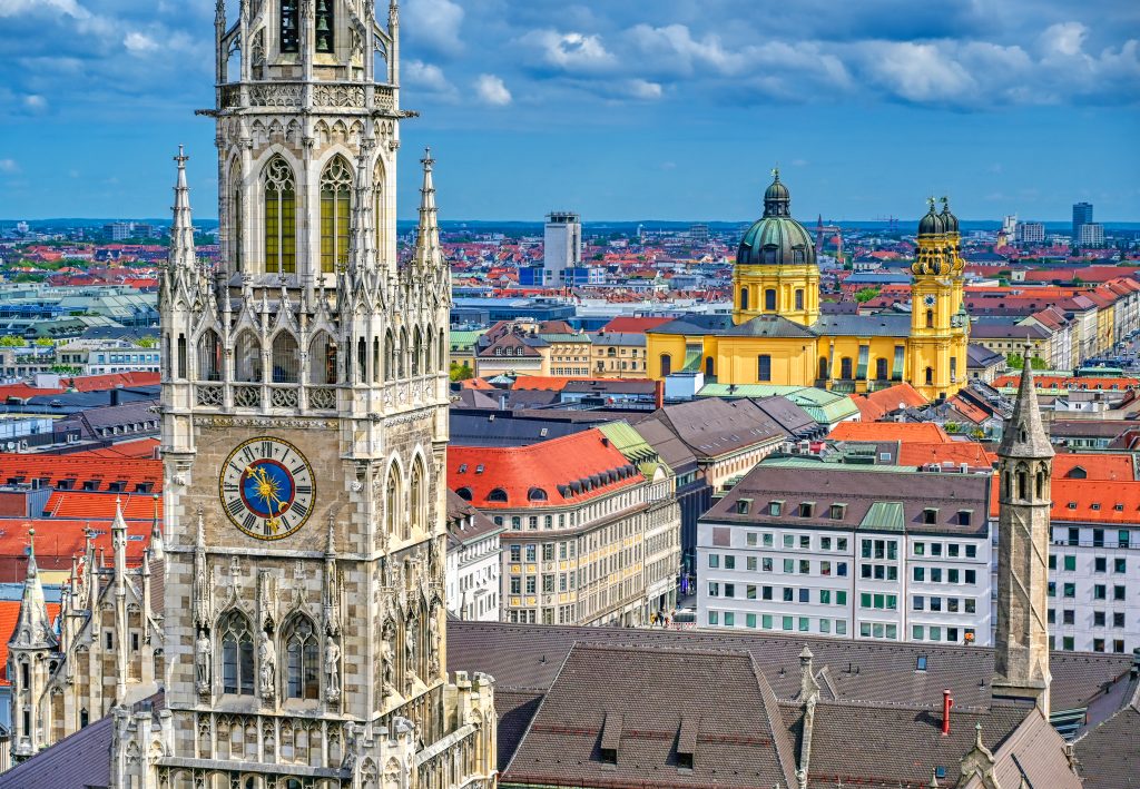 The cityscape of Munich, Germany, showing the historic Marienplatz architecture and red-tiled roofs under a blue sky.
