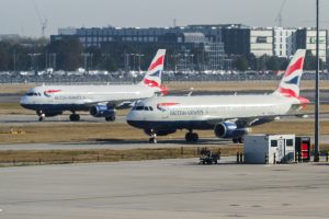 A line of British Airways commercial airplanes taxiing and parked on the airport tarmac.