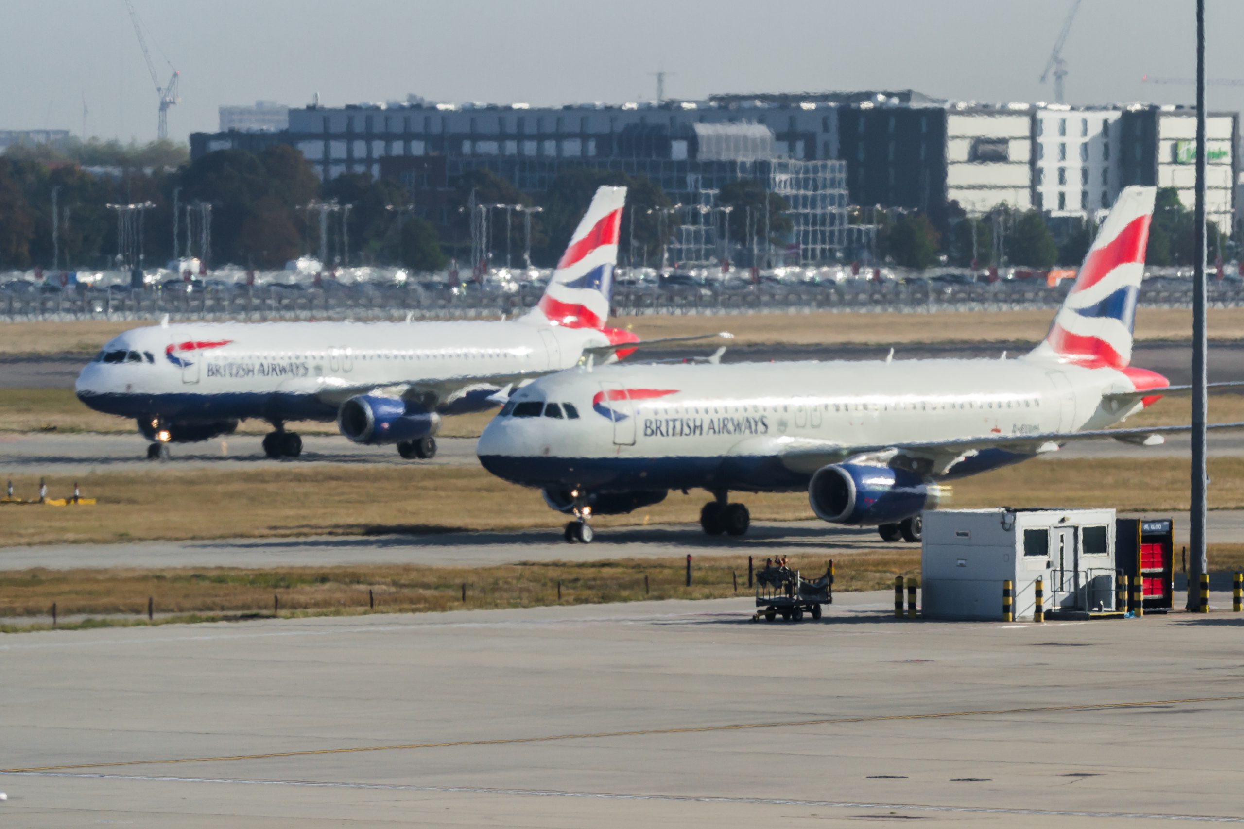 A line of British Airways commercial airplanes taxiing and parked on the airport tarmac.