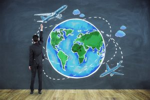 A businessman stands at a chalkboard, drawing flight paths on a chalk illustration of a globe and two airplanes, representing a global VIP Airport Service.