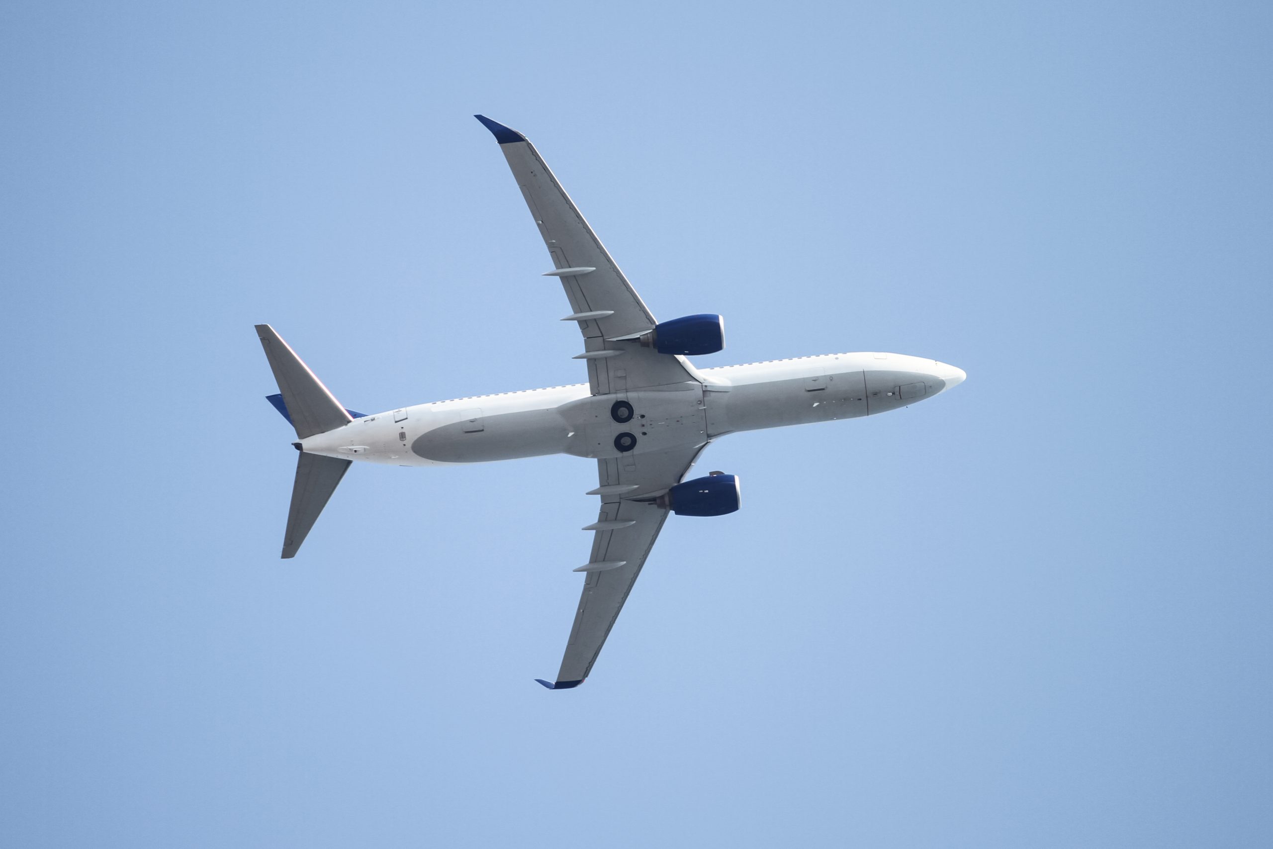 An airplane (jetliner) viewed from underneath as it climbs after takeoff from Suvarnabhumi Airport, Bangkok, into a blue sky.