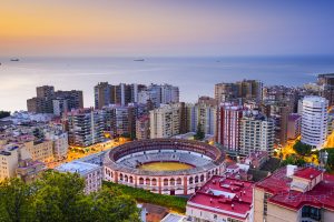 Malaga Airport travel destination view: Málaga skyline with La Malagueta bullring and Mediterranean coastline at sunset