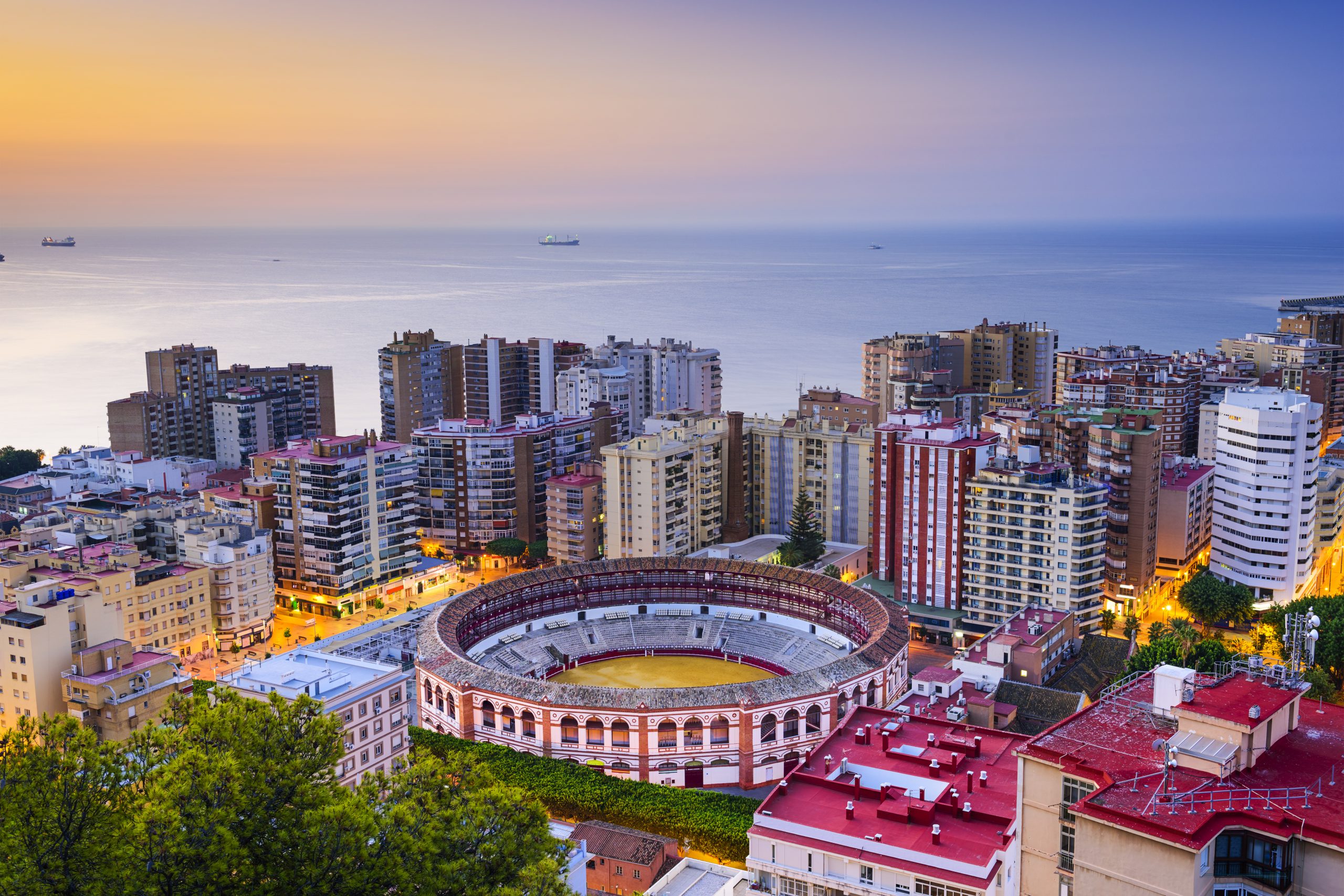 Malaga Airport travel destination view: Málaga skyline with La Malagueta bullring and Mediterranean coastline at sunset
