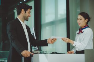Man in a suit hands a document to a receptionist behind a counter in a modern lobby.