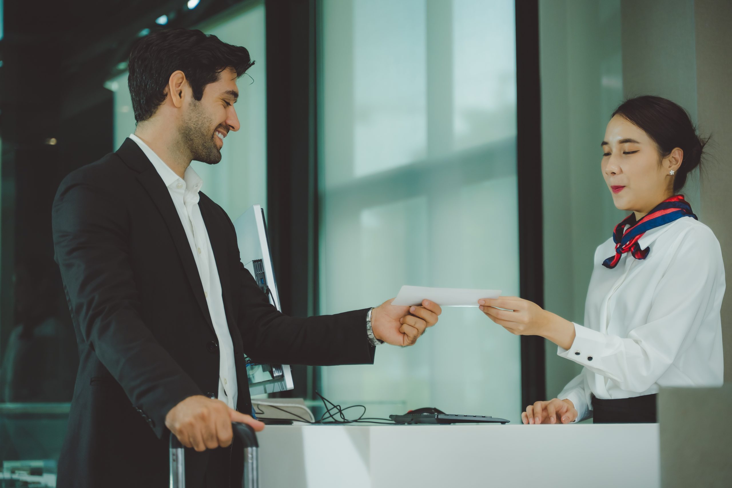 Man in a suit hands a document to a receptionist behind a counter in a modern lobby.