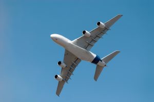 Four-engine white commercial airliner flying overhead, viewed from beneath against a clear blue sky